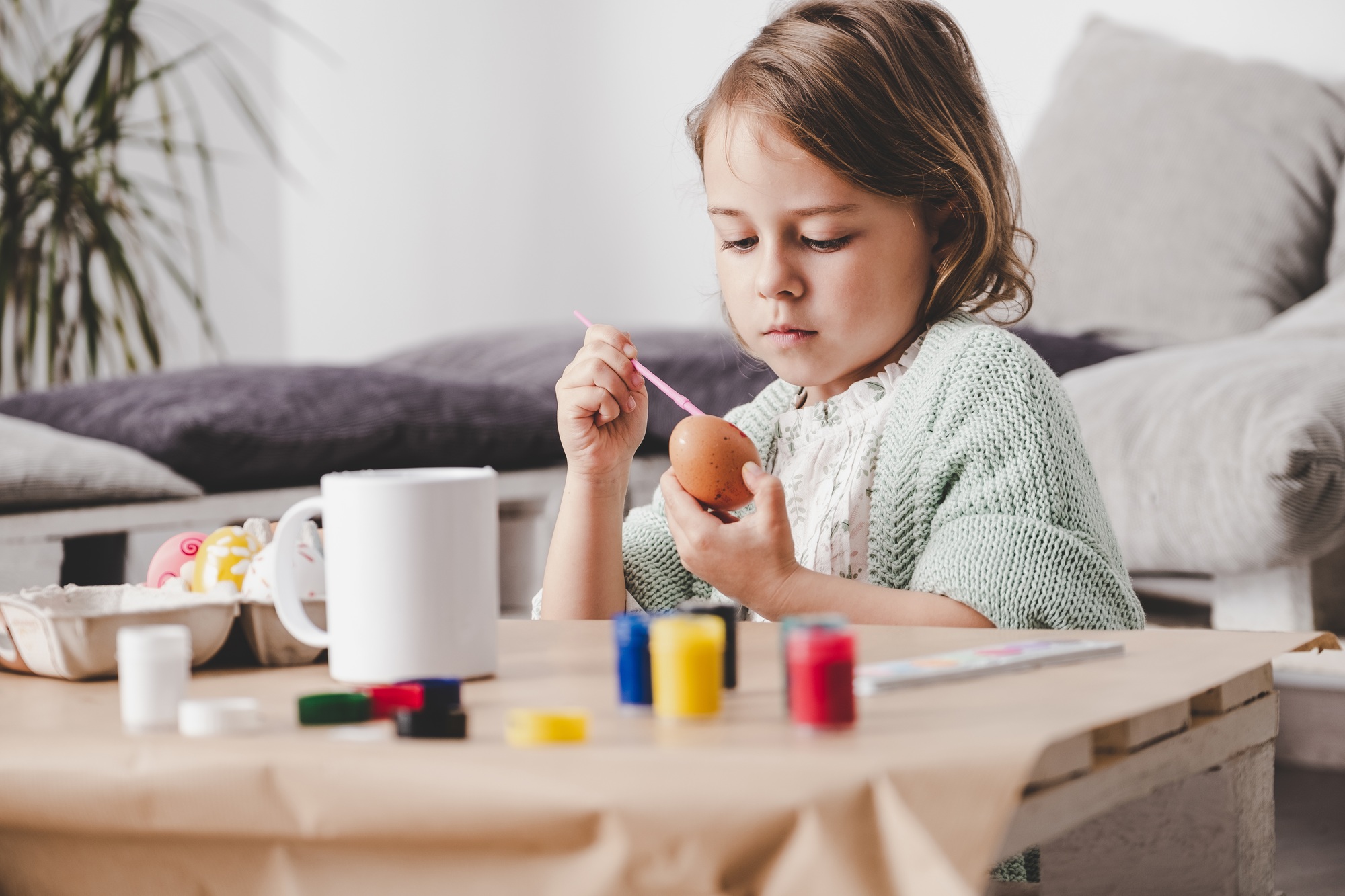 Girl coloring chicken egg at table