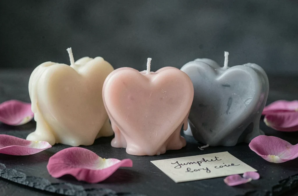 Trois bougies en forme de cœur posées sur ardoise avec des pétales de roses et une carte de condoléances manuscrite